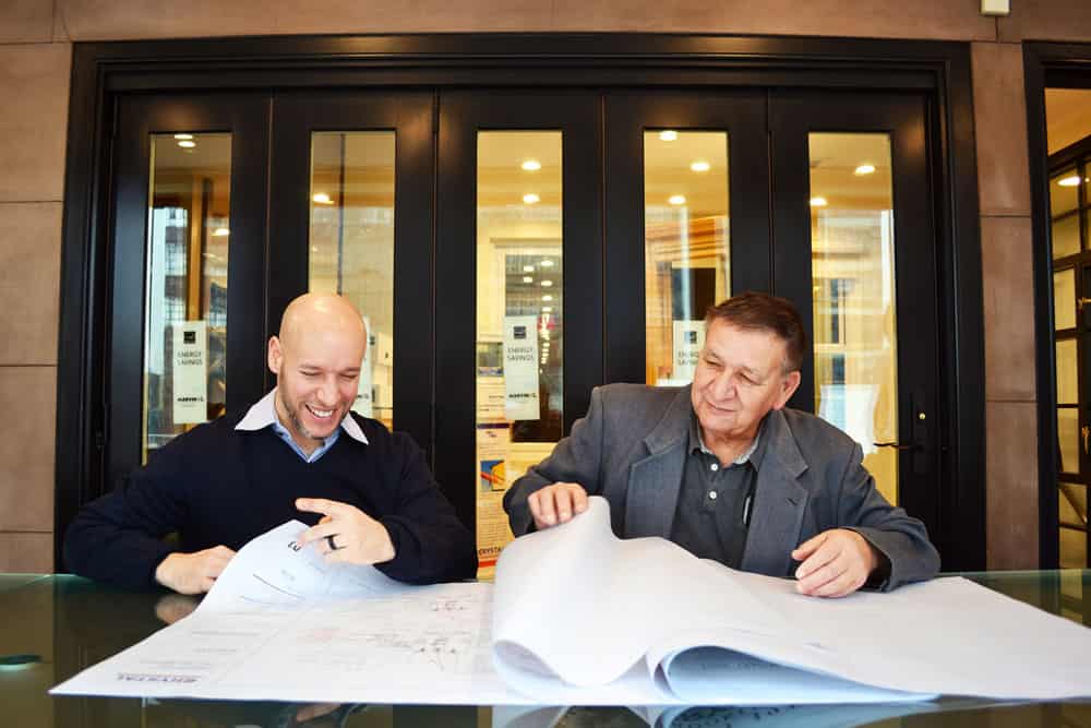 Two men sitting at a table looking at blueprints.