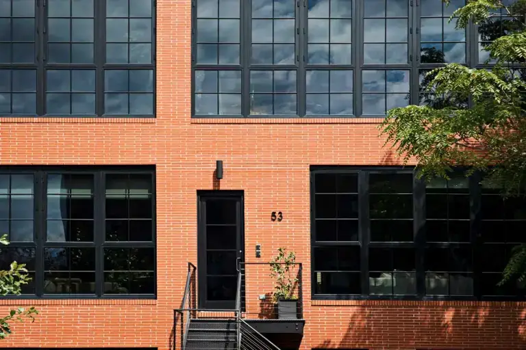 WindowFix - A modern brick building exterior with large black-framed windows, a black door with the number 53, metal steps, and a potted plant by the entrance.