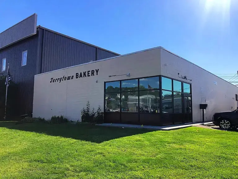 WindowFix - A single-story building with "Tarrytown BAKERY" on the side, large windows at the entrance, and a grassy lawn in front, under a clear blue sky.