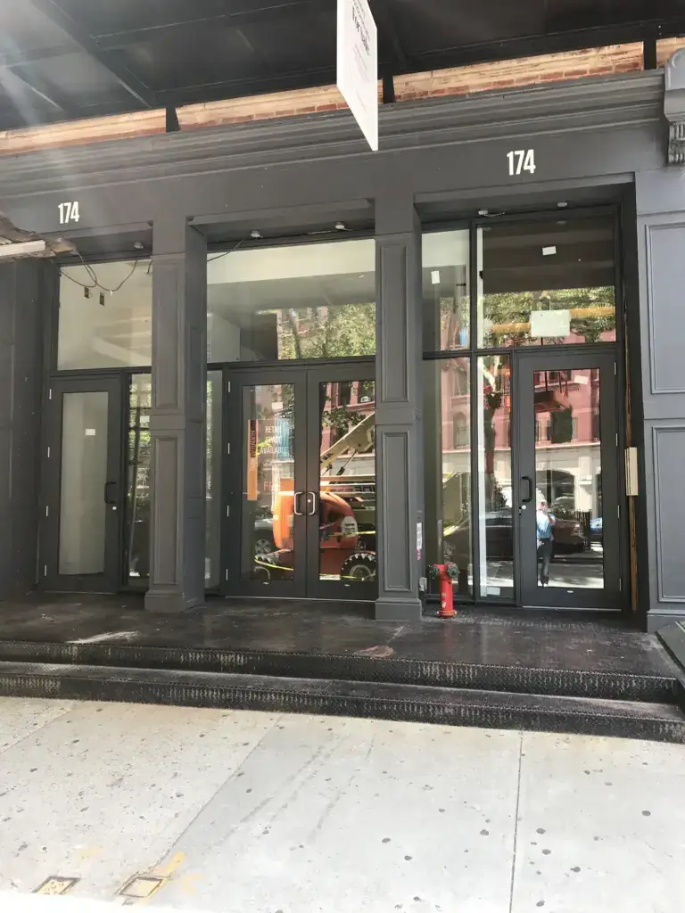 WindowFix - Street-level view of a modern black storefront with large glass doors and windows at 174, with a fire extinguisher placed on the entrance platform.