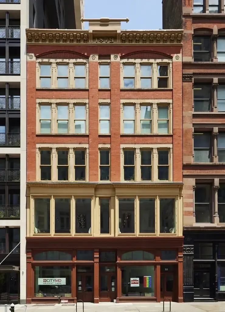 WindowFix - A five-story red brick building with an updated facade, large windows, and decorative trim, situated between two taller buildings in an urban setting.