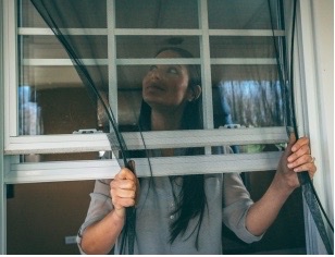 A woman placing a FlexScreen in her window opening.