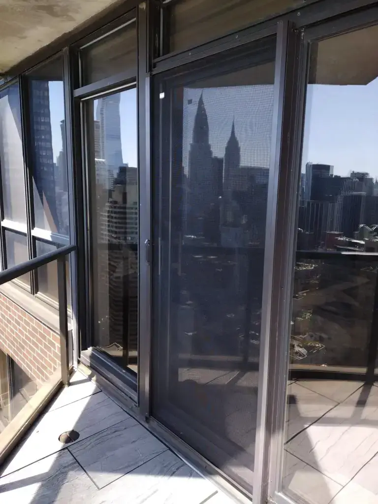 WindowFix - A glass balcony door with a mesh screen overlooks a cityscape with skyscrapers under a clear sky.