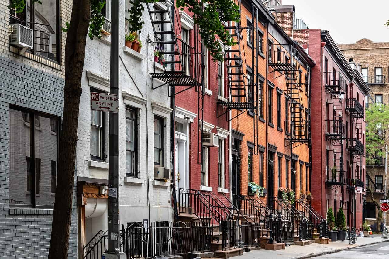 WindowFix - Row of brick and stone New York apartment buildings with black fire escapes along a quiet city street; “No Parking Anytime” sign visible.