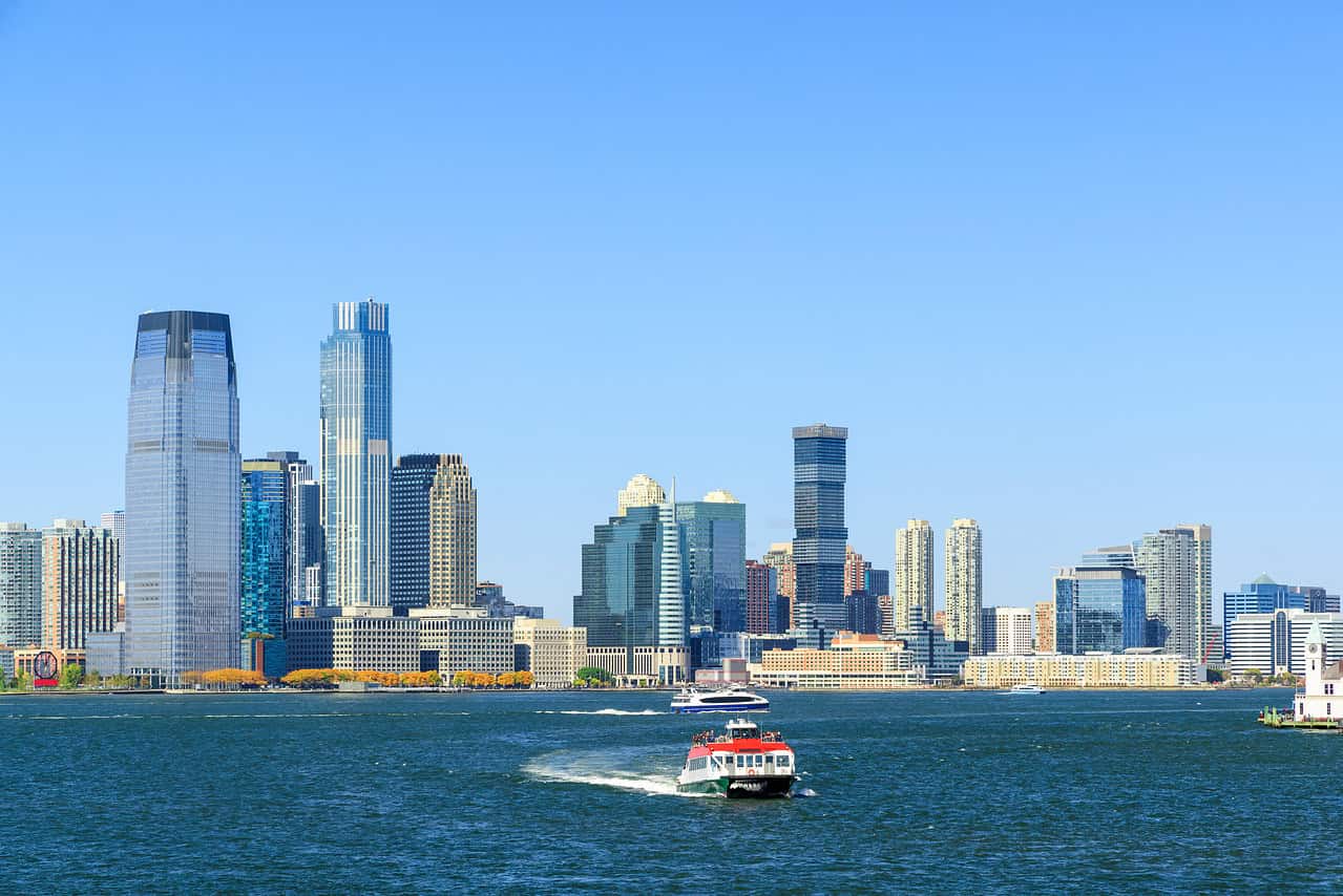 WindowFix - A white boat travels across a river with the New Jersey city skyline of tall buildings in the background under a clear blue sky.