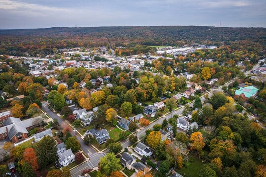 WindowFix - Aerial view of a New Jersey suburban neighborhood with tree-lined streets and houses, surrounded by autumn foliage and a forested hill in the background.